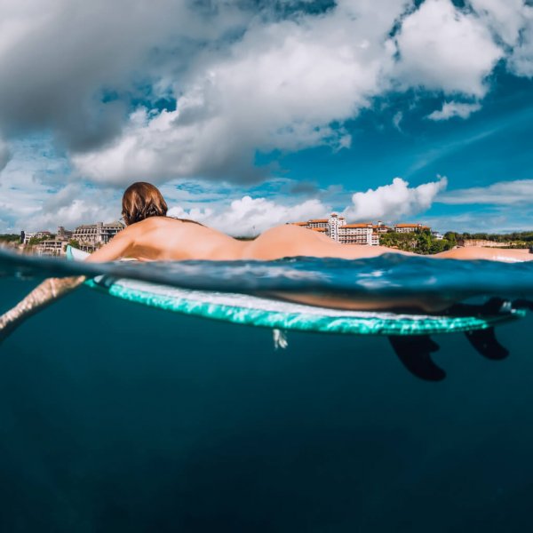 Surf girl floats on surfboard. Naked woman during surfing. Surfer and ocean