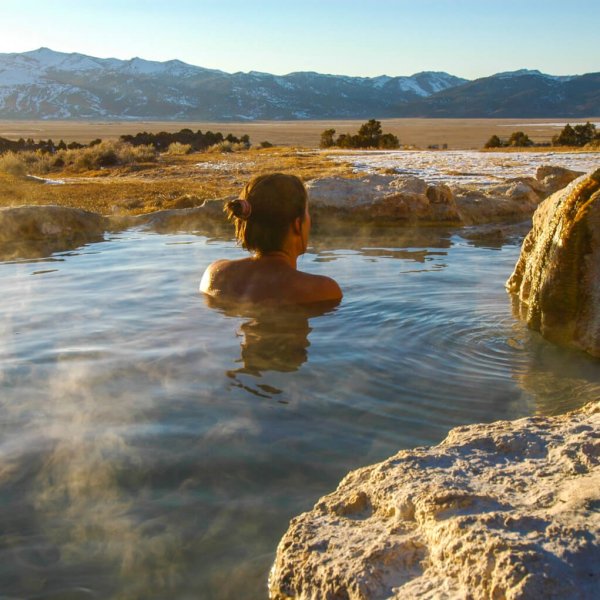 Woman enjoys view of Sierra Nevada Mountains while soaking in hot spring.